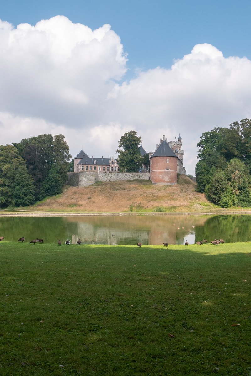 The turreted, ivy-hung silhouette of Gaasbeek Castle reflected in its moat, set in parkland near Brussels